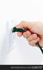 Hand inserting green electrical plug into outlet
