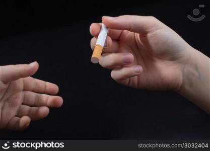 Hand is giving out cigarette on black background. Hand is giving out cigarette on a black background