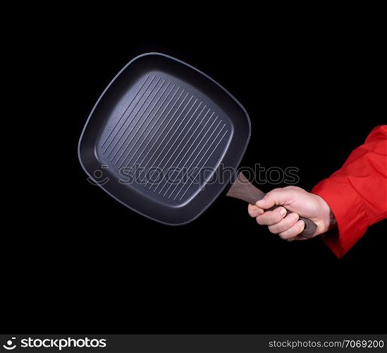 hand is holding a black empty square grill pan, black background