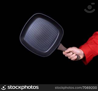 hand is holding a black empty square grill pan, black background
