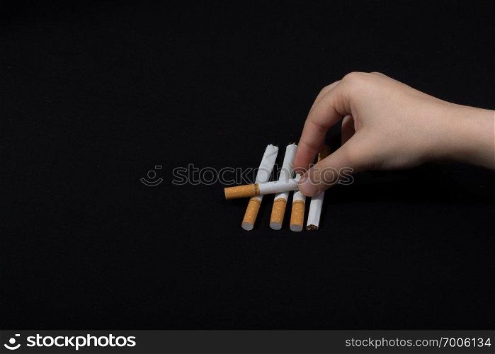 Hand is holding crossed cigarettes on black background