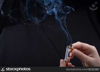 Hand is holding smoking cigarette on black background. Hand is holding smoking cigarette with smoke around