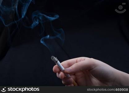 Hand is holding smoking cigarette with smoke around