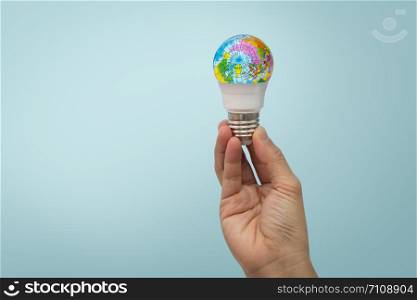 Hand is holding the LED bulb with the globe on blue background.