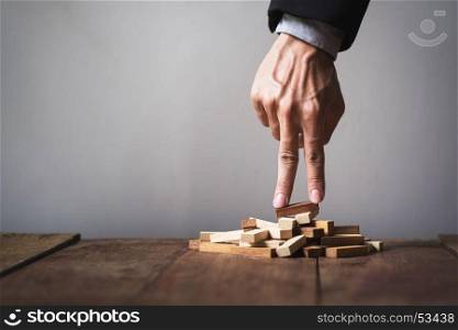 Hand liken business person stepping up a toy wooden block to goal