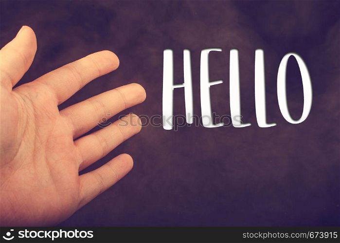 Hand making a hello welcome gesture on dark background