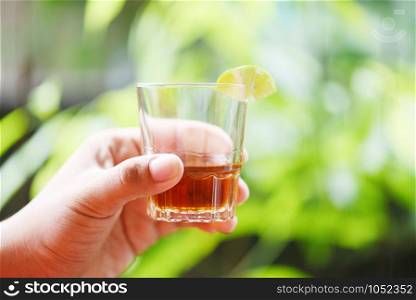 Hand man holding glasses of whiskey or alcohol drink with lemon lime and nature green background