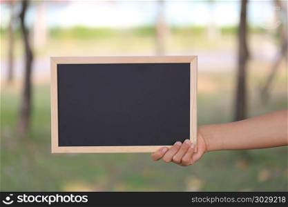 Hand of a business woman holding a empty black wooden picture fr. Hand of a business woman holding a empty black wooden picture frame on blur garden background and have copy space to input ideas in your work.