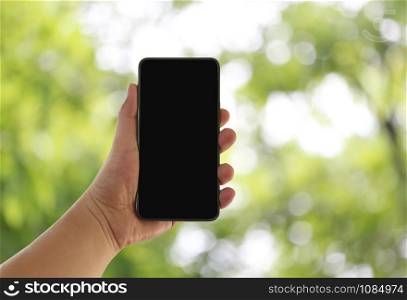 Hand of a businessman hold smartphone and empty screen on green nature blue background.