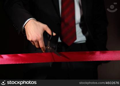 Hand of a businessman with scissors cuting a red ribbon