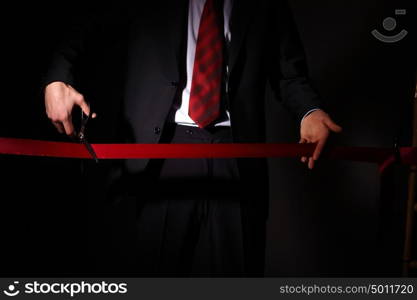 Hand of a businessman with scissors cuting a red ribbon