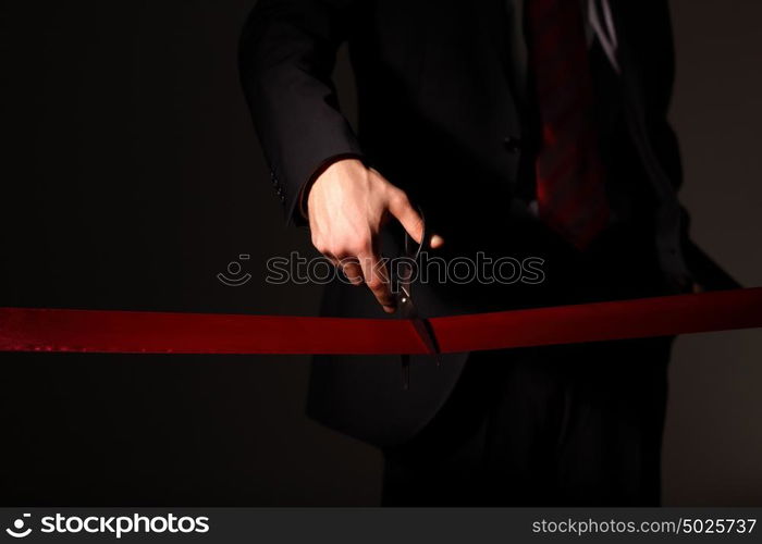 Hand of a businessman with scissors cuting a red ribbon