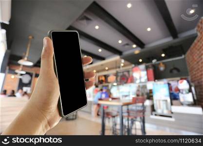Hand of a man holding smart phone device in the coffee cafe background and have copy space for design.