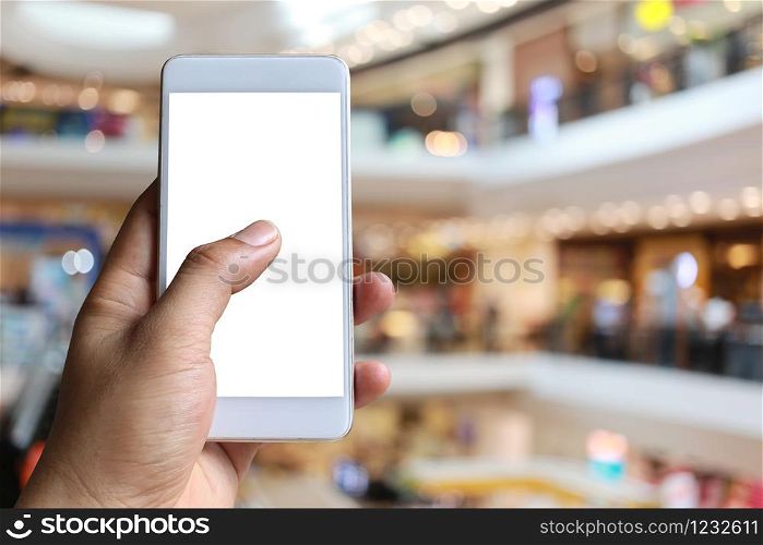 Hand of a man holding smartphone device in the Shopping mall background and have white copy space on screen.