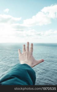 Hand of a man over a crystal clear horizon of the ocean with white clouds with copy space, inspiration and freedom concept