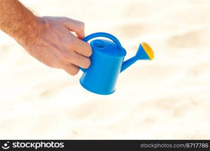 hand of a man with a watering can on a background of sand