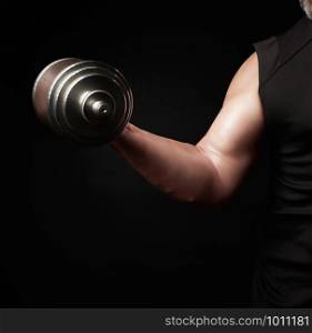 hand of a man with big biceps holds a steel type-setting dumbbell, low key, sports training with weight
