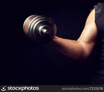 hand of a man with big biceps holds a steel type-setting dumbbell, low key, sports training with weight