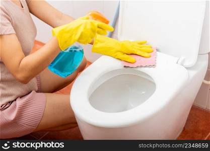 Hand of Asian woman cleaning toilet seat using liquid spray and pink cloth wipe restroom at house, female wearing yellow rubber gloves she sitting cleanup bowl bathroom, Housekeeper healthcare concept