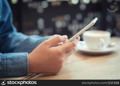Hand of asian woman using smartphone on wooden table in coffee shop