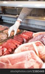 Hand of assistant picking meat in the supermarket at a fresh meat counter