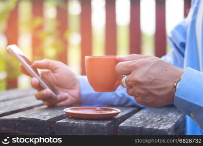 Hand of businessman holding a cup of coffee and playing smartphone,Vintage Style.