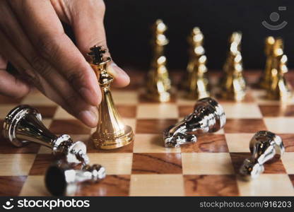 Hand of businessman moving golden chess figure for eliminating in battle competition with last successful ending game. Leadership strategy and management tactic concept. Wooden checkmate chessboard