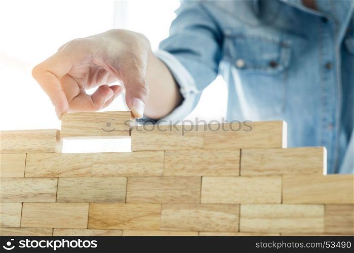Hand of engineer playing a blocks wood tower game (jenga) on blueprint or architectural project concept
