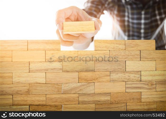 Hand of engineer playing a blocks wood tower game (jenga) on blueprint or architectural project concept