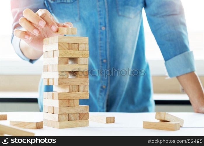 Hand of engineer playing a blocks wood tower game (jenga) on blueprint or architectural project