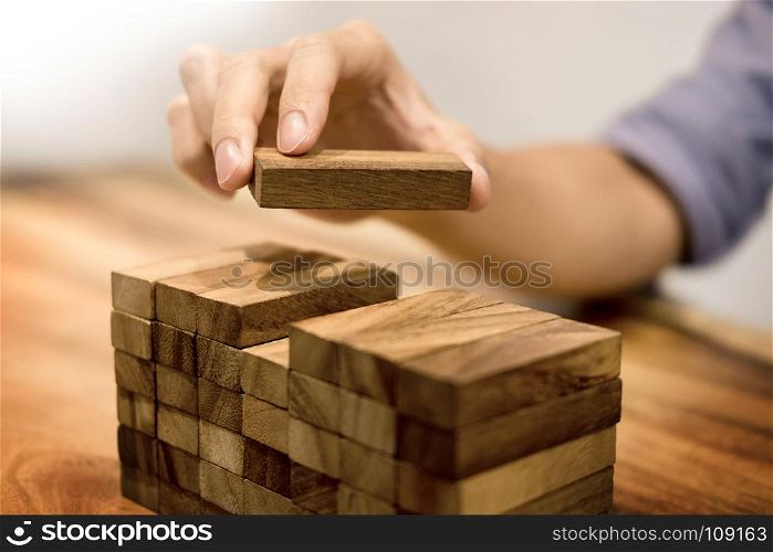 Hand of engineer playing a blocks wood tower game on blueprint or architectural project concept
