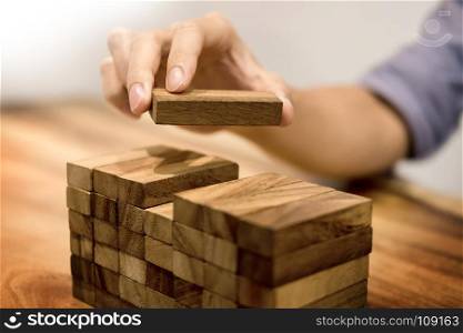 Hand of engineer playing a blocks wood tower game on blueprint or architectural project concept