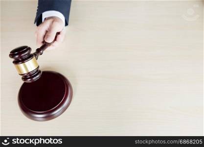 hand of Judge&rsquo;s holding wooden hammer knocking a gavel against wooden background.