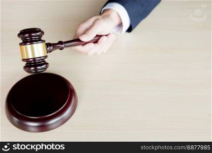 hand of Judge&rsquo;s holding wooden hammer knocking a gavel against wooden background.