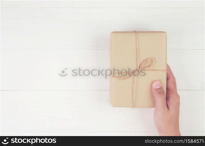 Hand of man holding gift giving on wooden table in Christmas day or holiday, present box for anniversary or birthday or celebration with copy space, celebrate and festive, top view, flat lay.