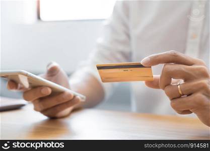 Hand of man in casual shirt paying with credit card and using smart phone for online shopping making orders via the Internet using mobile bank application, Online payment