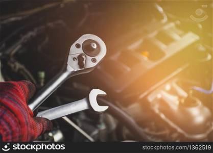 Hand of mechanic professional man hold a wrench tools with car engine blurred background in vehicle repair garage,Automotive maintenance concept.