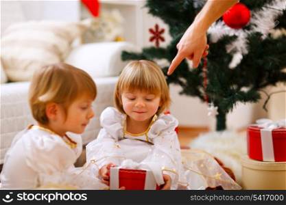 Hand of parent pointing on present to twins girl&#xA;