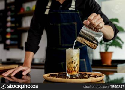 Hand of person pouring milk In coffee drink on wooden plate in coffee shop Thailand selective focus blur background