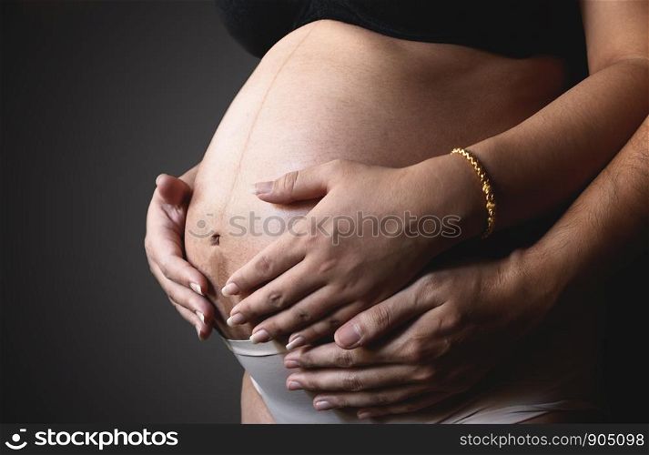 Hand of pregnant woman and husband hugging the tummy.
