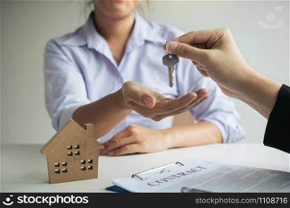 Hand of real estate agent passes the key to new homeowners in office with buyer house concept.