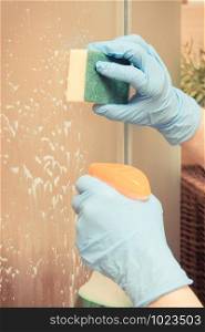 Hand of senior woman in protective gloves using sponge with detergent for washing and cleaning glass shower door. Hand of senior woman using sponge with detergent for washing and cleaning glass shower