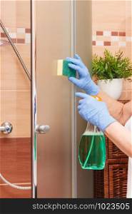 Hand of senior woman in protective gloves with sponge and detergent cleaning glass shower door, concept of household duties. Hand of senior woman with sponge and detergent cleaning glass shower door, household duties concept