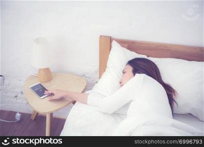 Hand of sleepy woman waking up with alarm clock on mobile phone in bedroom.