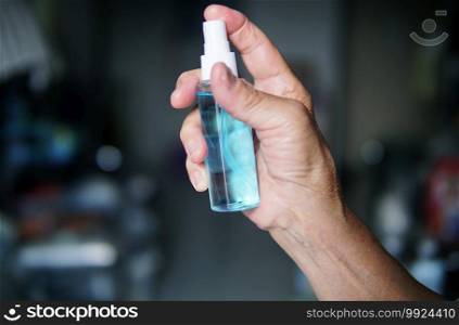 Hand of the elderly woman with alcohol spray bottle.
