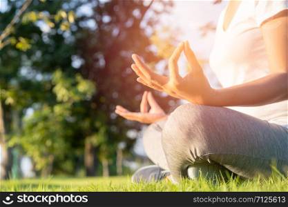 Hand of woman in lotus pose sitting on green grass and blurred background in the park, Concept of relaxation and meditation