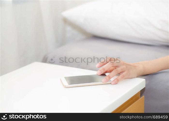 hand of woman turn off alarm on call mobile phone while wake up after sleep relax in good morning at bedroom.