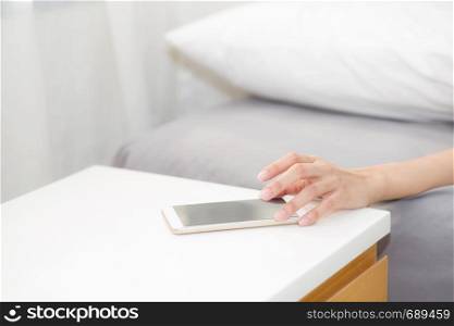 hand of woman turn off alarm on call mobile phone while wake up after sleep relax in good morning at bedroom.