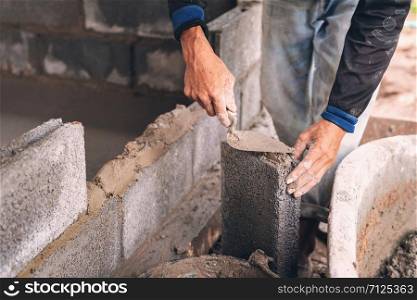 hand of worker plastering cement on brick wall at construction site