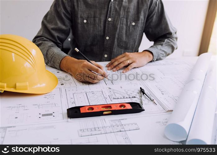 Hand of young engineering man drawing on blueprint at table in office room.